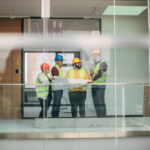 Group of architects and engineers at construction site discussing building plans while holding blueprint.